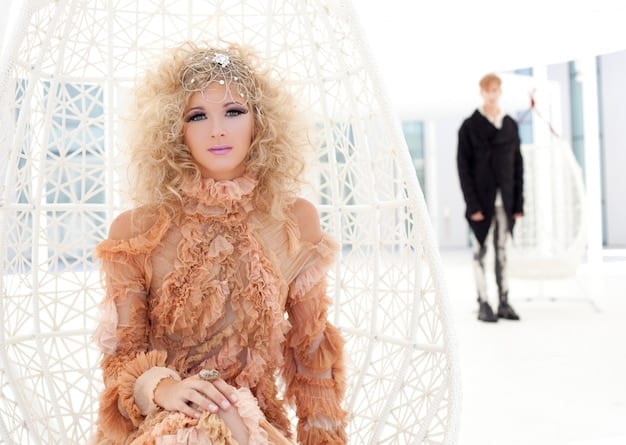 A fashion runway scene with a model wearing a full-length dress made of intricately woven natural fibers. The dress features a complex pattern with geometric and organic shapes. The model is walking confidently, and the background is blurred to emphasize the dress and the craftsmanship it represents.