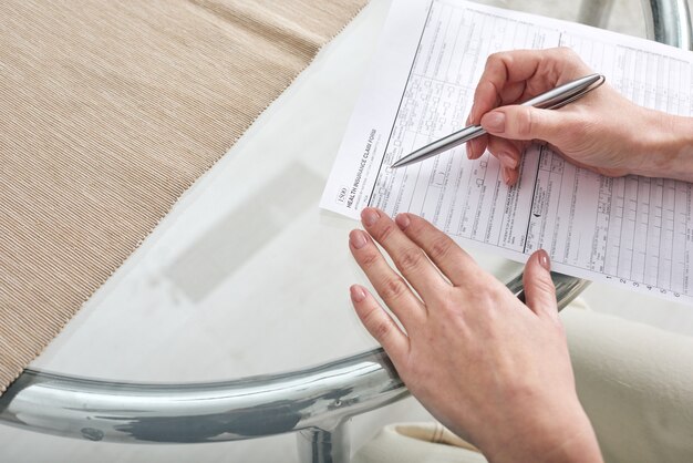 A close-up of a hand holding a government assistance form, with a pen resting on it. In the blurred background, there are papers and documents, suggesting bureaucratic processes. The image highlights the application aspect of the Ingreso Mínimo Vital.