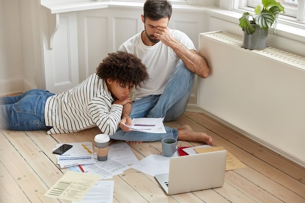A concerned parent looking over financial documents at home, with their child playing quietly in the background. The room is modestly furnished, highlighting the family's focus on essential needs.