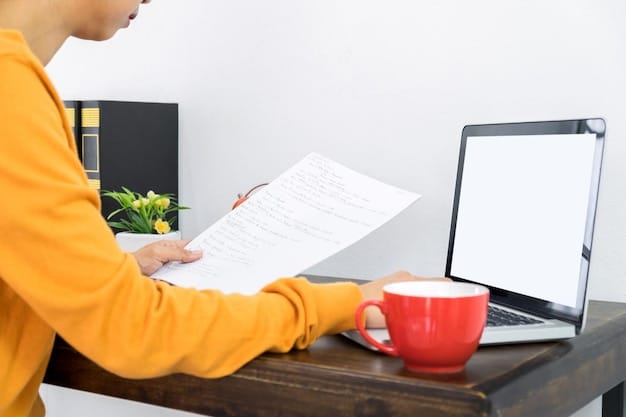 A person organizing documents and filling out a form on a wooden desk, with a laptop and a cup of coffee next to them.