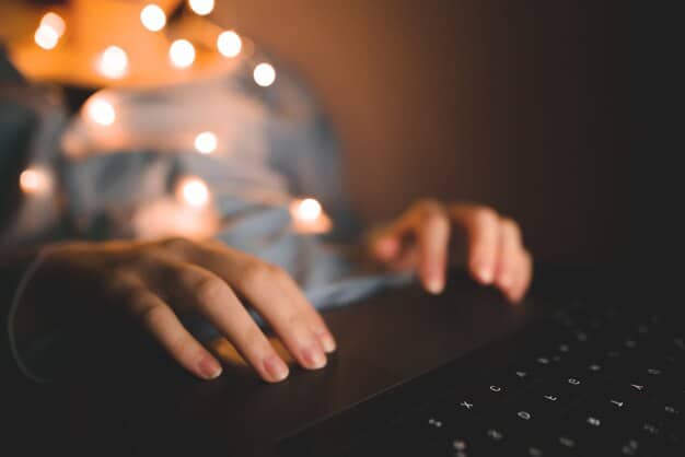 Hands typing on a laptop keyboard in a brightly lit office setting, with focus on the fingers and keys.