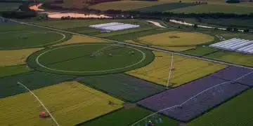 Vista aérea de uma paisagem agrícola moderna e produtiva ao pôr do sol, com sistemas de irrigação avançados e culturas diversas, simbolizando o agronegócio em 2026.