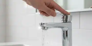 Mão fechando uma torneira pingando, simbolizando a economia de água.